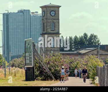 UK Weather: Glasgow, UK. 25th July, 2021. UK Weather: Another hot sunny day saw locals and tourists enjoy the sun with the inevitability of It ending sometime soon. The distinctive clock tower of the Glasgow distillery company and its clydeside location makes it a favourite for locals keen to exercise on riverside path of the clyde walkway with crown plaza hotel in the background.. Credit: gerard ferry/Alamy Live News Stock Photo