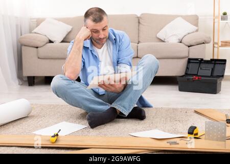 Puzzled Man Reading Furniture Assembly Manual Installing Shelf At Home Stock Photo