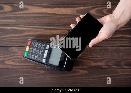 Top view of customer paying online from smartphone using modern easy nfc technology, holding cellphone with blank screen Stock Photo