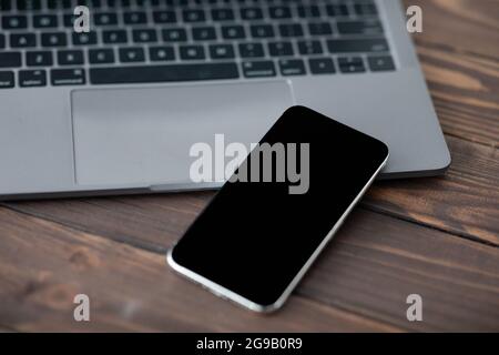 Modern smartphone with black blank screen placed near laptop computer, closeup. Mockup for your design or advertisement Stock Photo