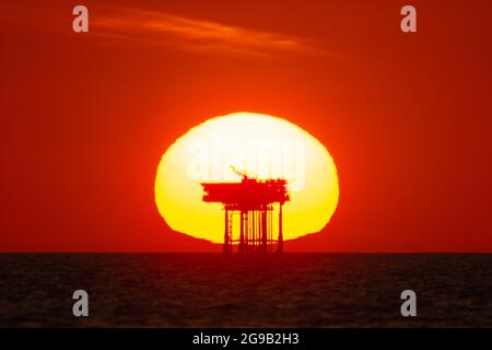 View of the sun setting behind an offshore oil/gas platform or rig at sea. Concept or theme of fossil fuels, petrochemicals, sunset industry Stock Photo
