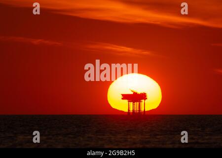View of the sun setting behind an offshore oil/gas platform or rig at sea. Concept or theme of fossil fuels, petrochemicals, sunset industry Stock Photo