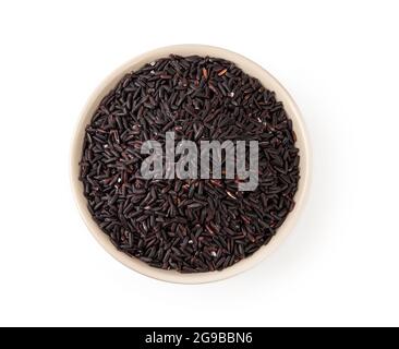 Raw black rice in a beige ceramic bowl isolated on white background. Unpolished organic black rice as source of complex carbohydrates. Top view. Stock Photo