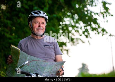 Smiling active senior man cycling or biking outside, choosing or selects the trip using the map, healthy lifestyle sport concept Stock Photo