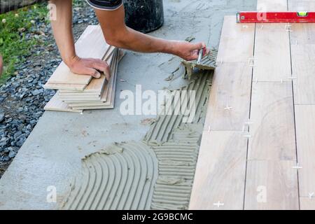 The hands of the professional tiler lying or installing modern, ceramic tile above cement on the garden terrace , tiling floor, building and pavement Stock Photo
