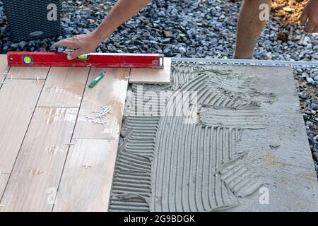 The hands of the professional tiler lying or installing modern, ceramic tile above cement on the garden terrace , tiling floor, building and pavement Stock Photo