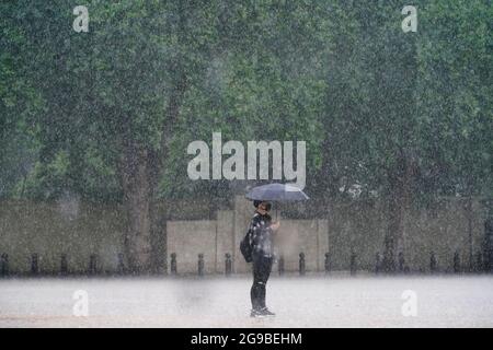A woman stands in the rain in Horse Guards Parade, Westminster as heavy rain sweeps through central London. Thunderstorms bringing lightning and torrential rain to the south are set to continue until Monday, forecasters have said. Picture date: Sunday July 25, 2021. Stock Photo