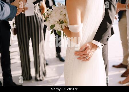 Groom hugs bride with a bouquet while standing in front of the guests Stock Photo