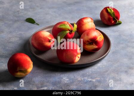 Several ripe peaches or nectarines lie on a black ceramic plate Stock Photo