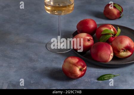 Peaches or nectarines on a black ceramic plate and glass of white wine Stock Photo