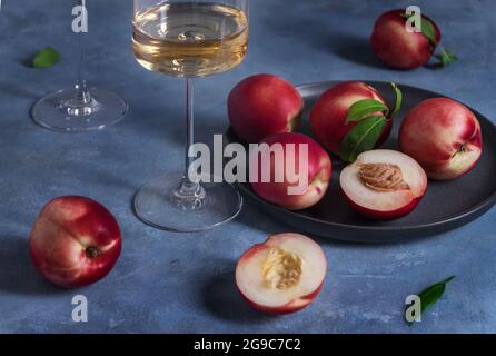 Peaches or nectarines on a black ceramic plate and glass of white wine Stock Photo
