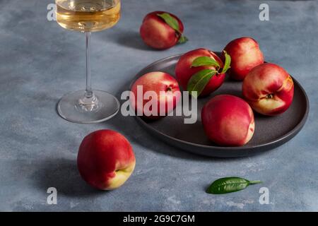 Peaches or nectarines on a black ceramic plate and glass of white wine Stock Photo