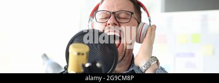Young man in headphones singing into microphone. Emotional singing concept Stock Photo