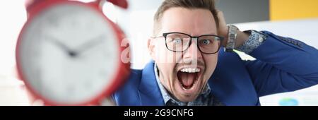 Young man holding alarm clock and shouting Stock Photo