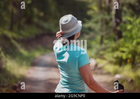 Mature woman walking in pine forest alone . Sunshine shining through the forest. Concept of travel and freedom. Selective focus Stock Photo