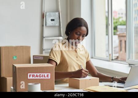 Portrait of young African-American woman using laptop in warehouse while managing small business, copy space Stock Photo