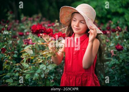 Beautiful little girl in roses garden in park. Charming woman smiling outdoor with flowers. Stock Photo