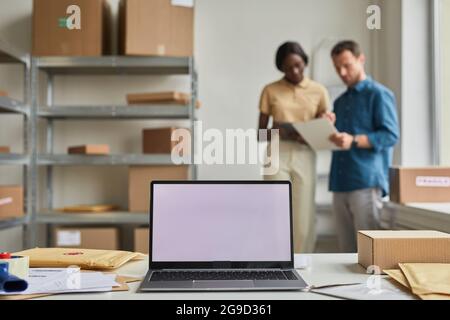 Background image of opened laptop with blank screen in warehouse interior with blurred workers, copy space Stock Photo