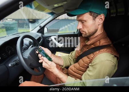 Side view portrait of man using smartphone with navigation app while sitting in car or van, copy space Stock Photo