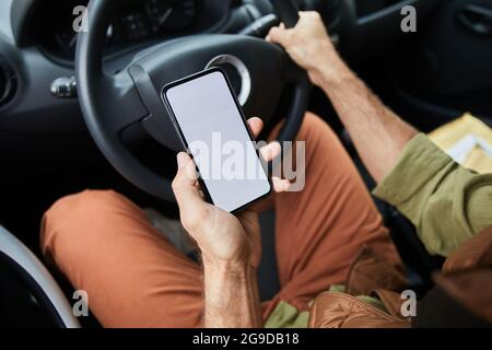 Close up of unrecognizable man driving car or van focus on hand holding smartphone with blank screen, copy space Stock Photo