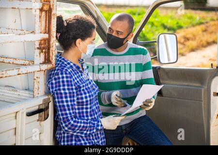 Farmer couple in protective masks discussing papers near car Stock Photo