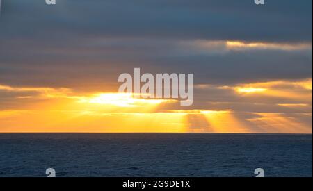 Sun rays passing through dark clouds. The unpredictable drama of the sky at sunset. A view from a tourist cruise ship sailing in the North Pacific Oce Stock Photo