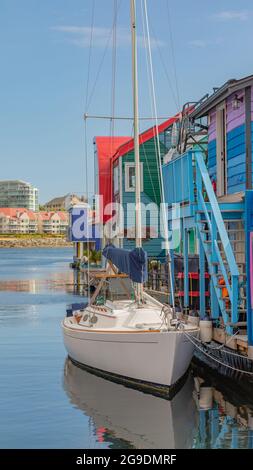 Beautiful morning view of the moored yacht on a pier by colorful boathouses in the Fisherman Wharf Village Victoria, BC, Canada. July 23, 2021. Street Stock Photo
