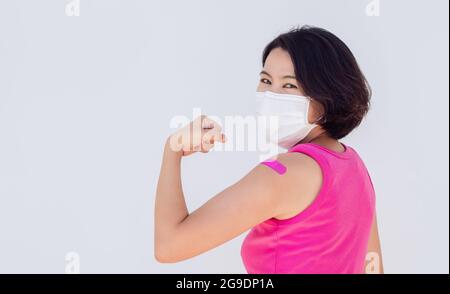 Vaccinations, bandage on vaccinated people banner concept. Asian woman wearing mask with bandage plaster showing strong gesture with fist hand after v Stock Photo