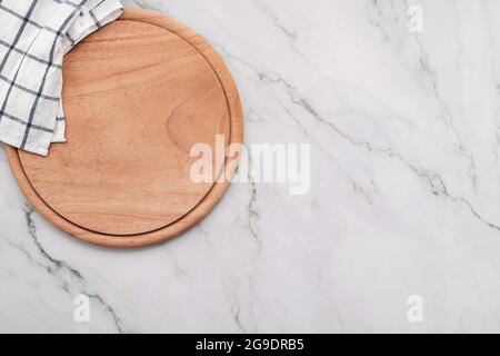 Empty wooden pizza platter with napkin  set up on marble stone kitchen table. Pizza board and tablecloth on white marble background. Stock Photo