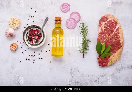Raw Striplion Steak set up on white concrete background. Flat Lay of fresh raw beef steak with rosemary and spice on white shabby concrete background Stock Photo