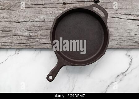 Empty old cast iron skillet set up on white marble  background with flat lay and copy space. Stock Photo