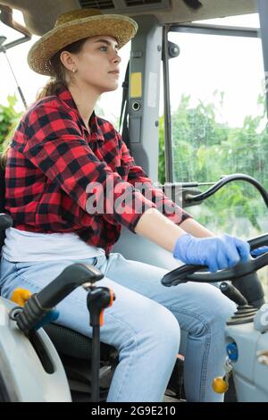 Skilled young female farmer working on small tractor in orchard Stock Photo