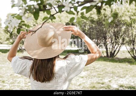 Pretty and young woman is posing on the green background. Beautiful and cute girl in the spring park. Attractive model in straw hat. Nice young female Stock Photo
