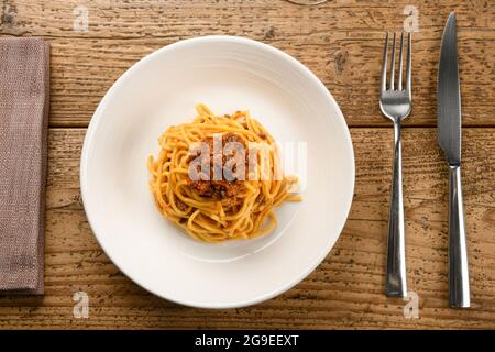 Serving of Tagliolini Italian pasta with wild boar ragout on a white ceramic plate with cutlery and napkin on a rustic wooden table in a top down view Stock Photo