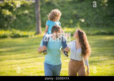 Happy family of mother and father carrying boy child on shoulders summer outdoors, foster Stock Photo