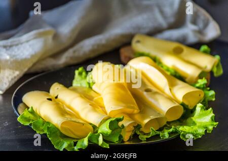 hard cheese with big holes sliced on a plate with lettuce leaves Stock Photo