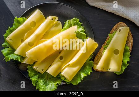 hard cheese with big holes sliced on a plate with lettuce leaves Stock Photo