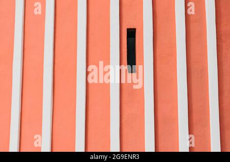 Red wall with vertical relief white stripes and narrow window Stock Photo