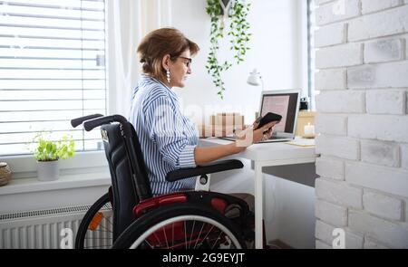 Disabled mature woman with laptop working indoors in home office, small business concept. Stock Photo