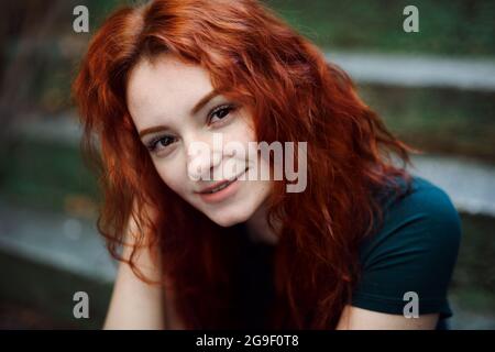 Portrait of young woman sitting outdoors on staircase in city, looking at camera. Stock Photo