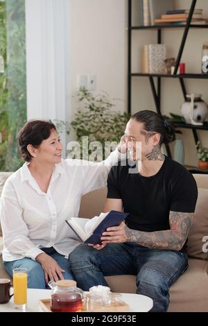 Mature mother talking to her elder son while they sitting on sofa in the living room Stock Photo