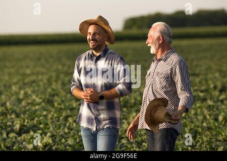 Handsome young farmer wearing straw hat laughing. Senior farmer holding straw hat in hand talking smiling. Stock Photo