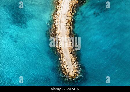 Aerial top down view of stone breakwater in bright blue sea surface. Stock Photo