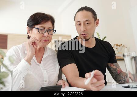 Elder son sitting at the table together with his mother, hey discussing finance together and paying for bills Stock Photo
