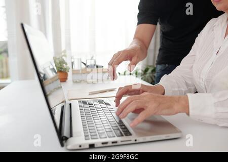 Close-up of woman sitting at the table and typing on laptop she working online with her colleague helping her in work Stock Photo