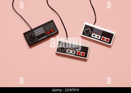 Three retro vintage game console controllers on a pastel pink background with copy space and room for text. Stock Photo