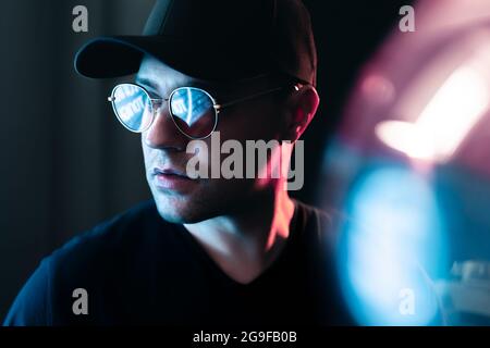 Neon light in glasses of a man. Futuristic cyber studio portrait. Techno glow and vibrant cyberpunk color. Male model with sunglasses. Stock Photo