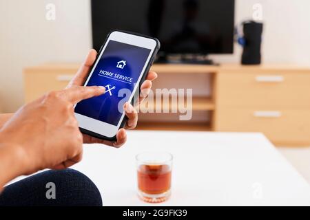 Hands of woman using home service app on her smartphone to call plumber or electrician Stock Photo