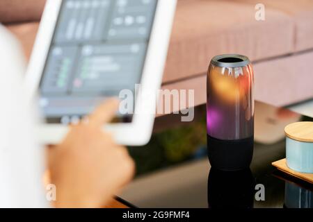 Woman connecting loudspeaker to smart home application on tablet computer to choose music and control volume via app Stock Photo