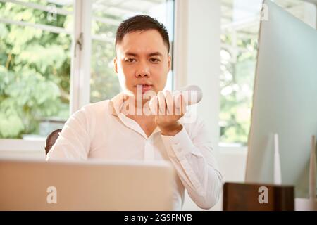 Young businessman reading e-mails or reports on laptop screen and recording voice message for coworker Stock Photo